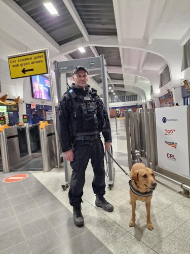 Lancashire police officer stood in front of a knife arch with a drug dog, at Blackpool north train station.